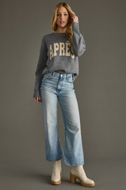 Woman wearing a gray sweater with 'APRES' text and blue jeans on a gray background
