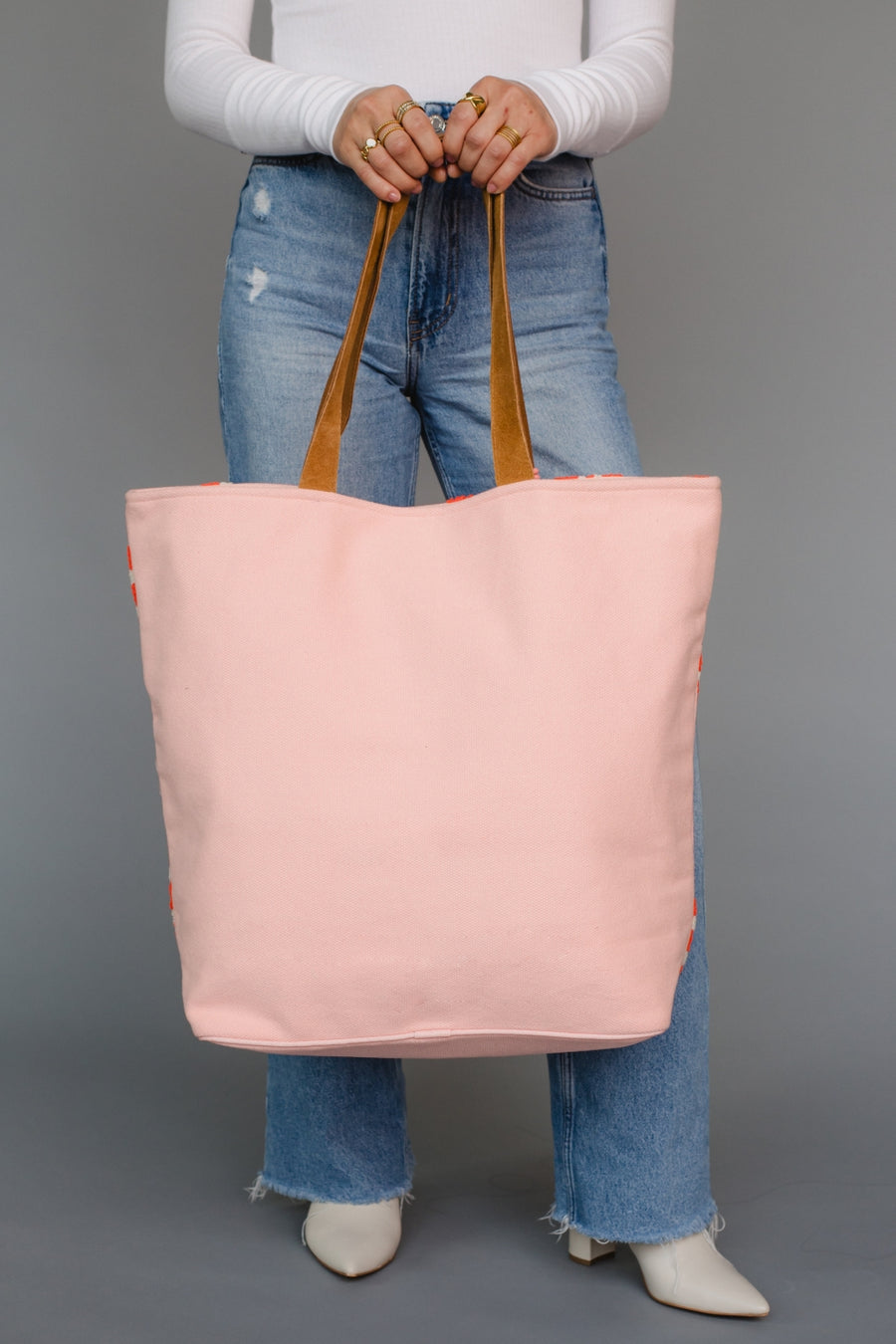 Person holding a pink tote bag with brown handles against a gray background