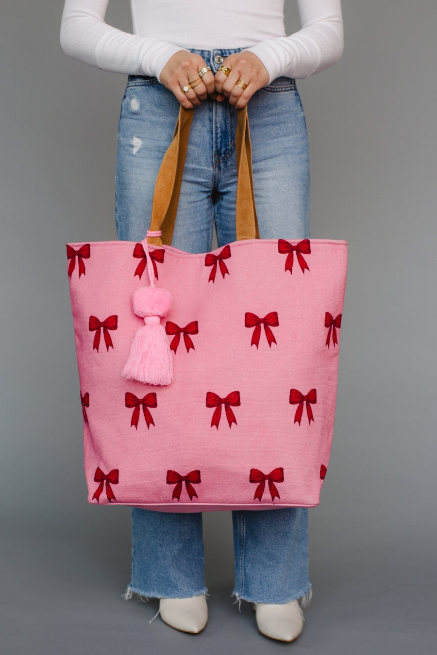 Person holding a pink tote bag with red bow patterns against a gray background