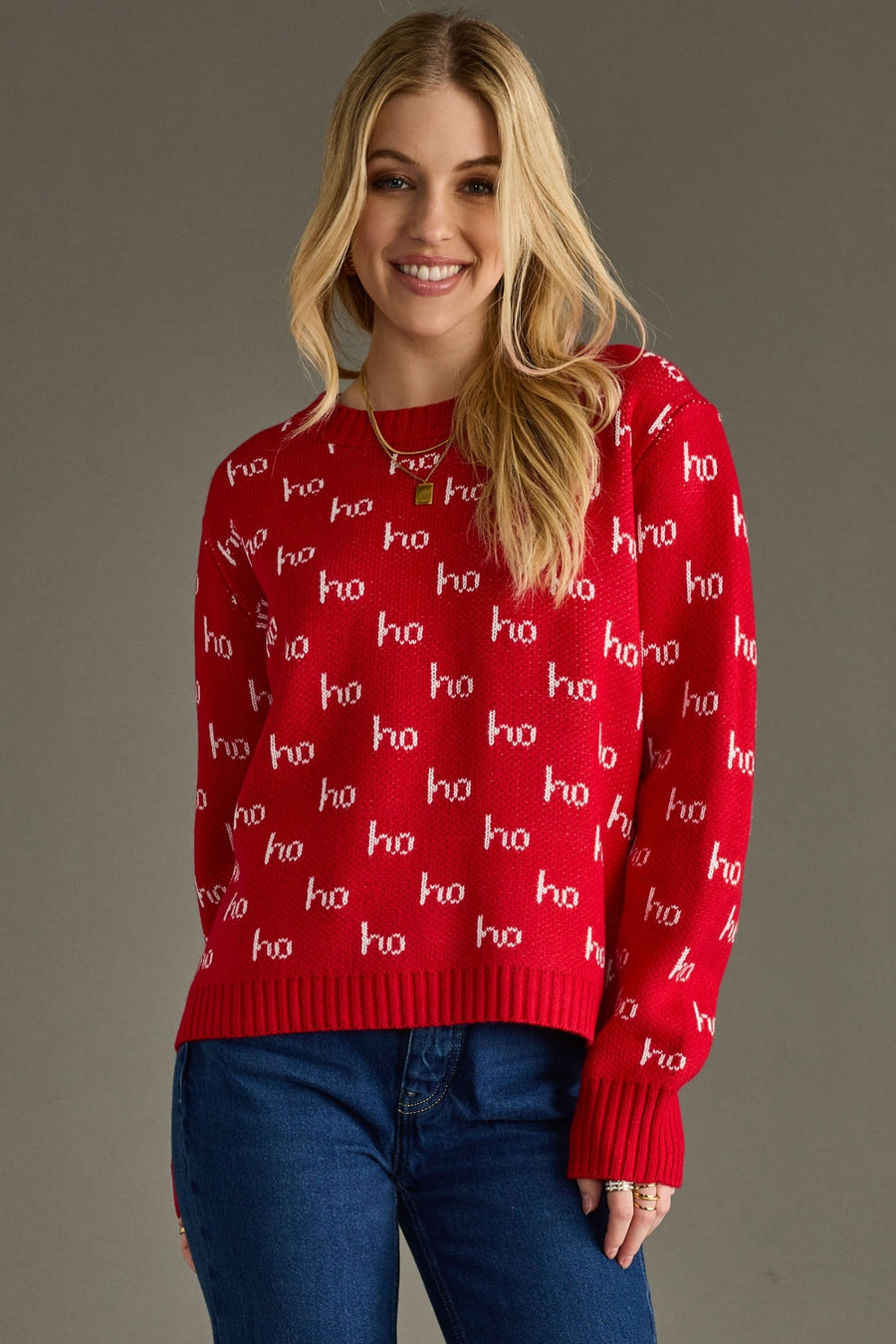 Woman wearing a red sweater with 'ho ho ho' pattern against a gray background