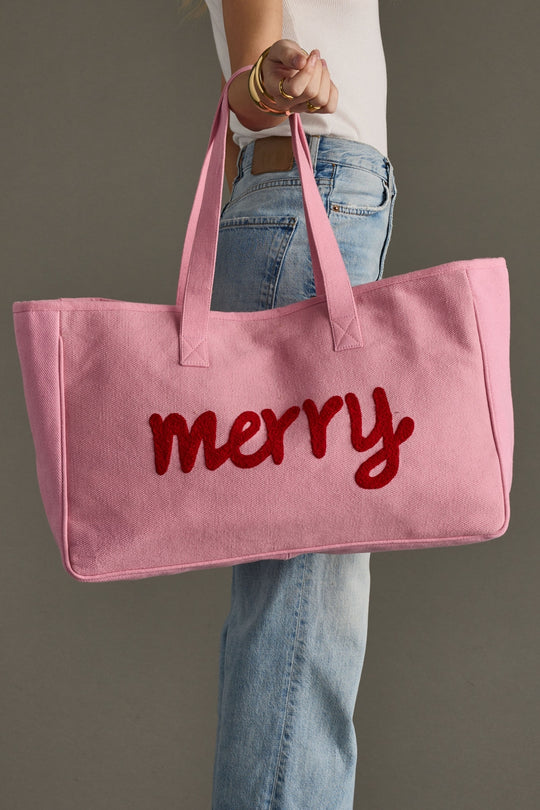 Pink tote bag with 'merry' text held by a person against a gray background