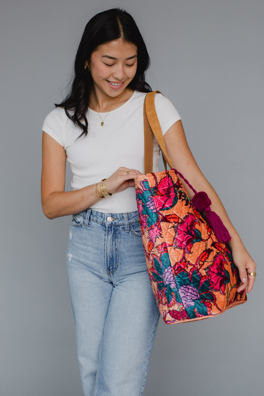 Woman holding a colorful floral tote bag against a gray background