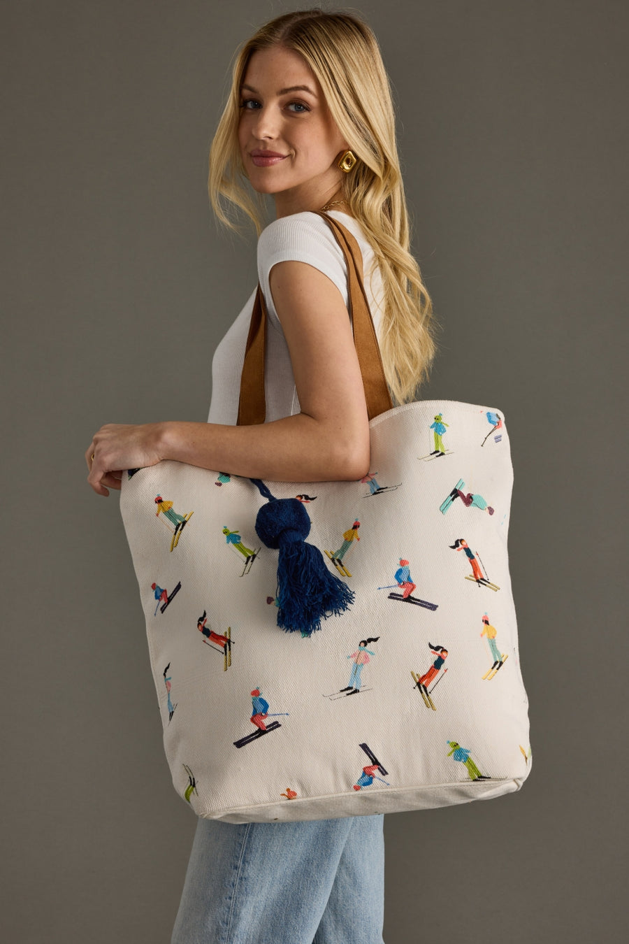 Woman holding a tote bag with skiing designs and a blue tassel.