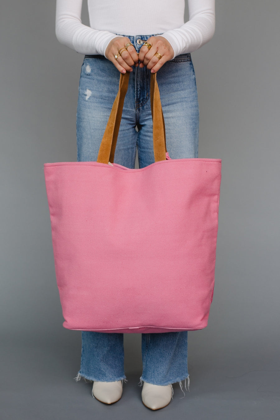 Person holding a pink tote bag with brown handles against a gray background