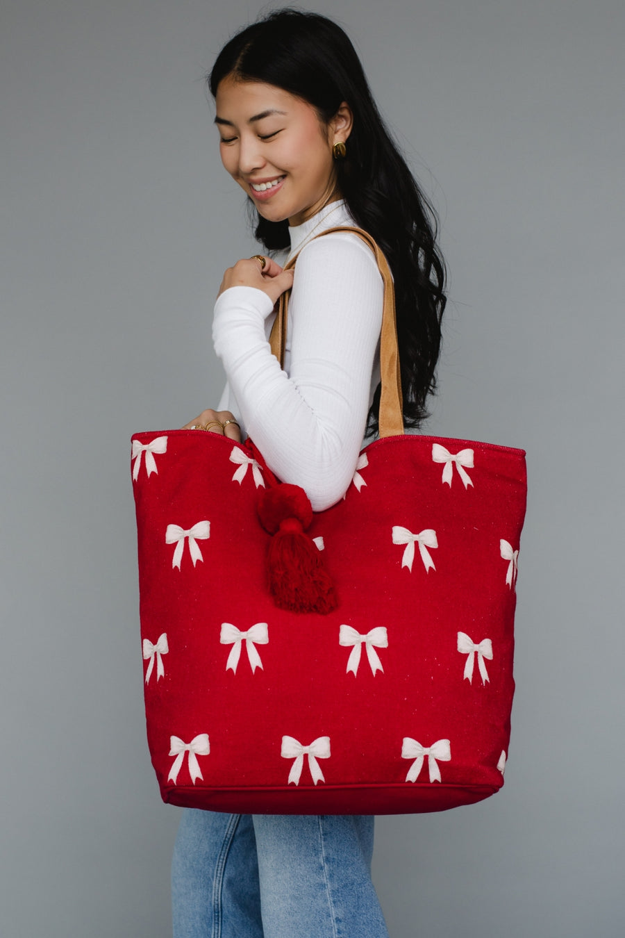 Woman holding a red tote bag with white bow patterns against a gray background