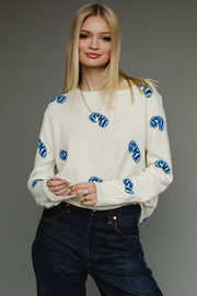 Woman wearing a white sweater with blue patterns on a gray background