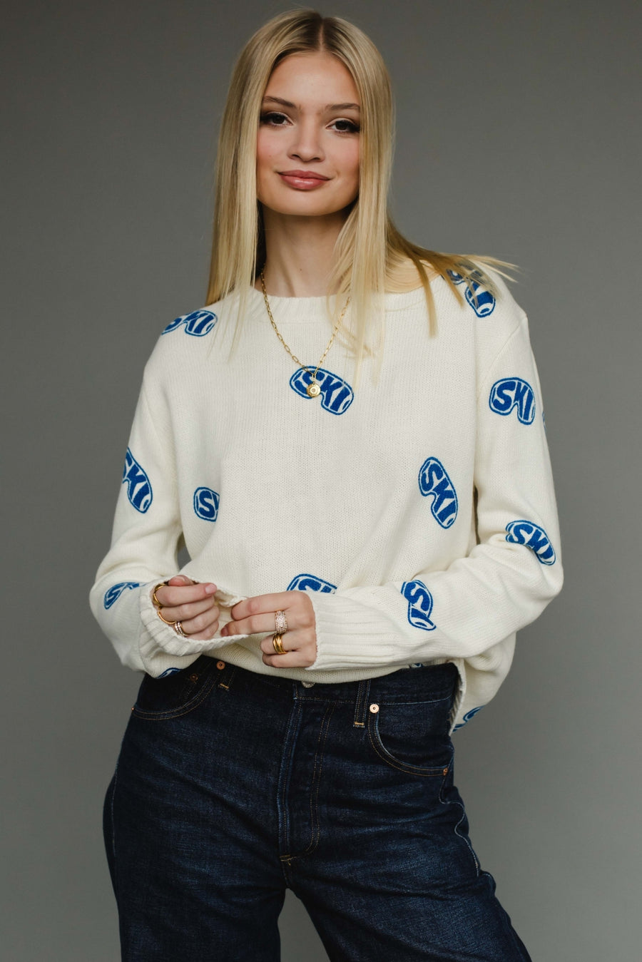 Woman wearing a white sweater with blue patterns on a gray background