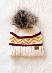 Knitted beanie with a fur pom-pom on a white textured background