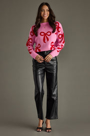 Woman wearing a pink sweater with red bows and black pants on a gray background