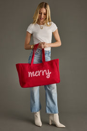 Woman holding a red tote bag with 'merry' on it against a gray background