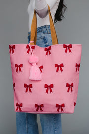 Pink tote bag with red bows and a pink pom-pom held by a person against a gray background