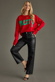 Woman wearing a red sweater with 'Merry' text and black pants on a gray background