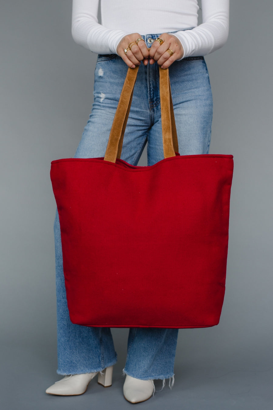 Person holding a red tote bag with brown handles against a gray background