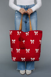 Red tote bag with white bow pattern held by a person against a gray background