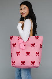 Person holding a pink tote bag with red bows against a gray background