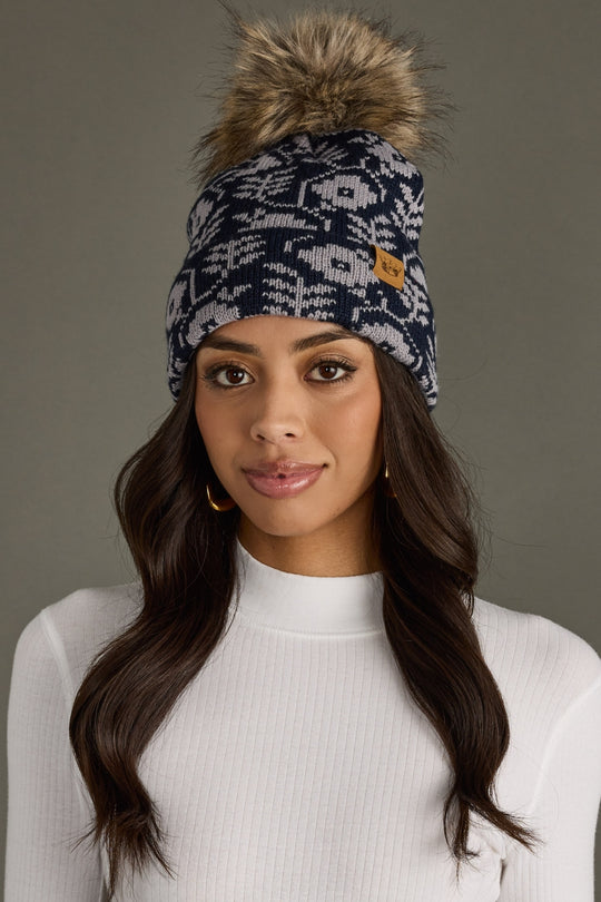 Woman wearing a patterned beanie with a fur pom-pom against a neutral background