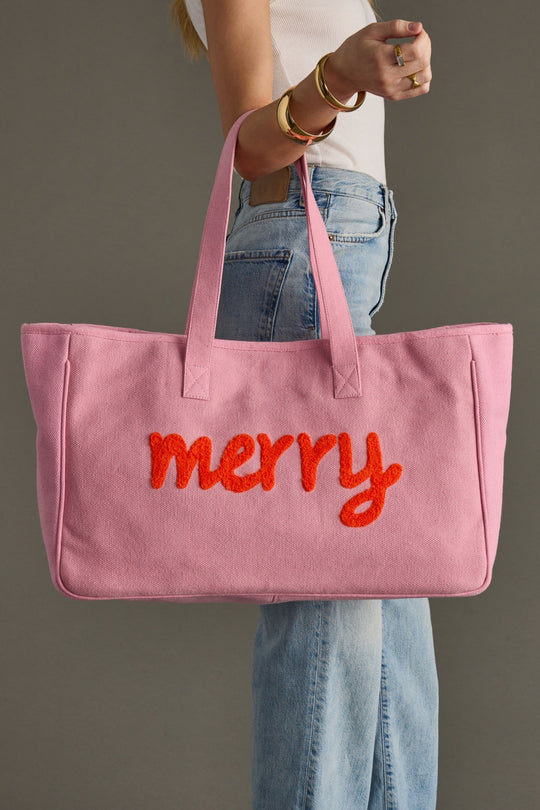 Pink tote bag with 'merry' text held by a person wearing jeans and a white shirt.