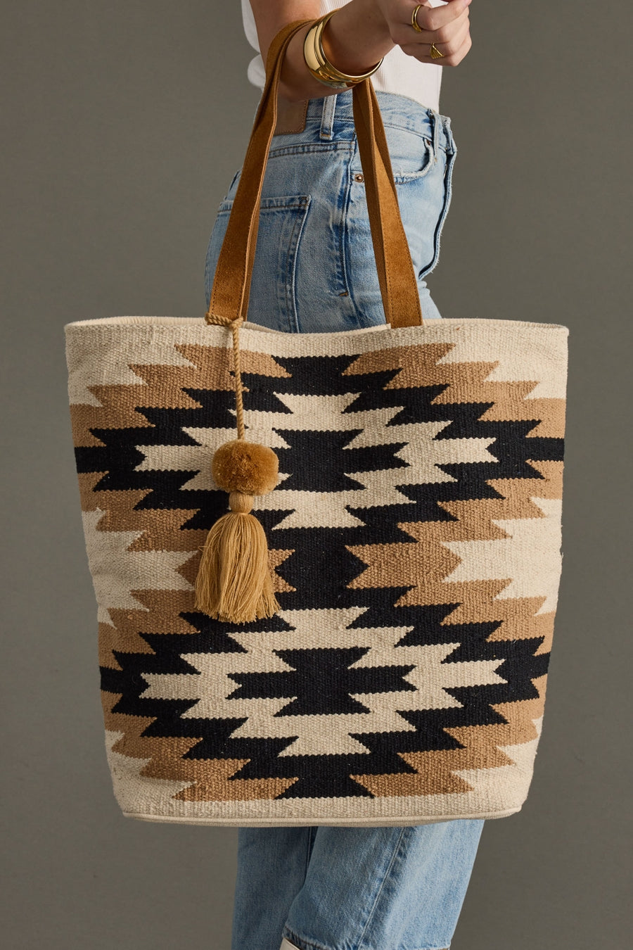 Tote bag with geometric pattern and tassel held by a person wearing jeans.