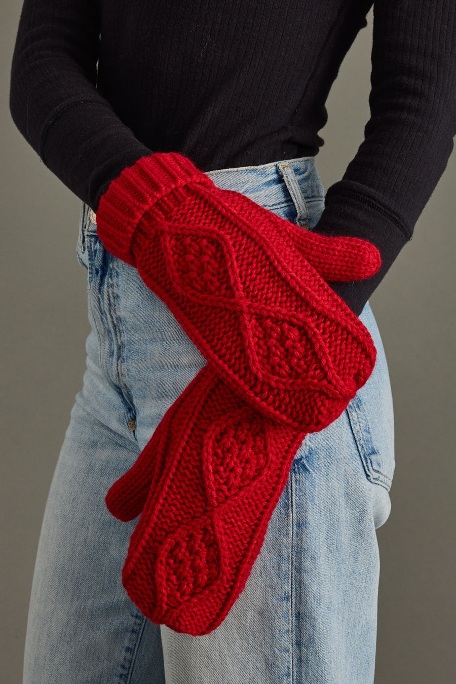 Red knitted gloves worn by a person against a neutral background