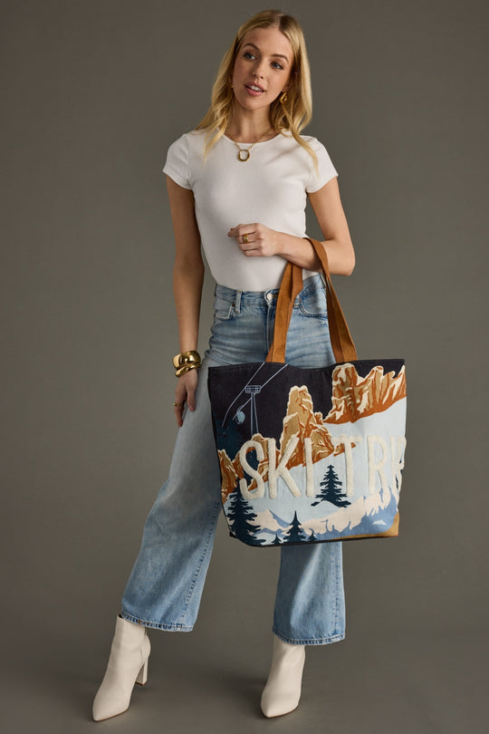 Woman holding a tote bag with a mountain design against a gray background