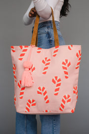 Pink tote bag with candy cane pattern held by a person against a gray background