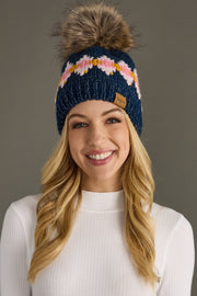 Woman wearing a blue knit beanie with a pom-pom against a gray background