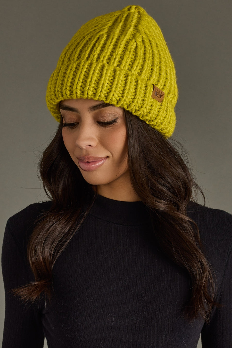 Woman wearing a lime green knit beanie against a gray background