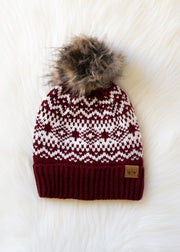 Knitted beanie with a pattern and fur pom-pom on a white textured background