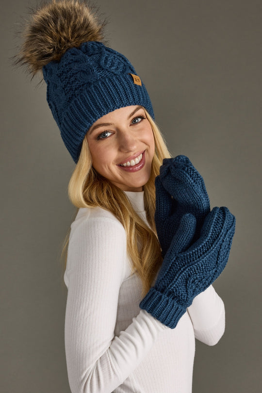 Woman wearing a blue knit beanie and gloves against a gray background
