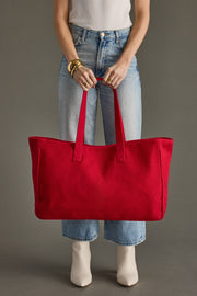 Person holding a red tote bag against a neutral background