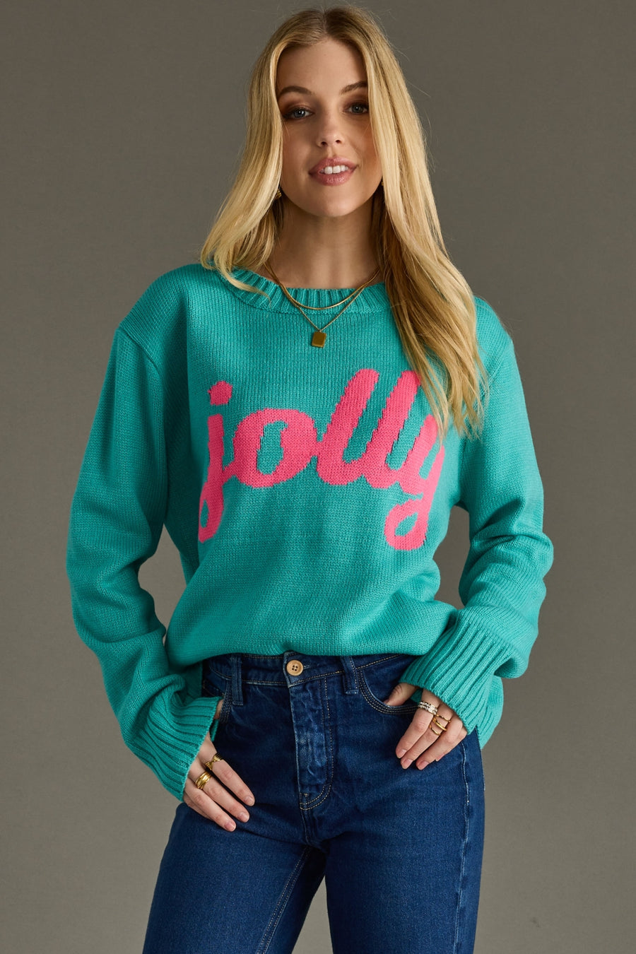 Woman wearing a teal sweater with pink text 'jolly' against a gray background