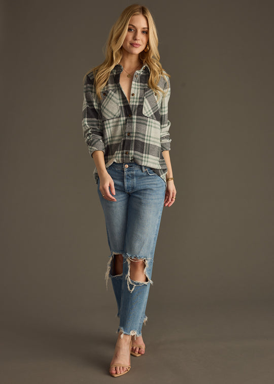 A woman with long blonde hair smiles slightly, wearing the panacheaccessories Dakota Super Soft Button Up and blue ripped jeans. One hand rests in her pocket, showcasing the shirts comfy, casual style against a plain background.