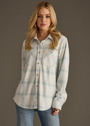 A woman with long blonde hair wears the panacheaccessories Jules Super Soft Button Up in light blue and white plaid, paired with blue jeans, standing against a plain brown background.