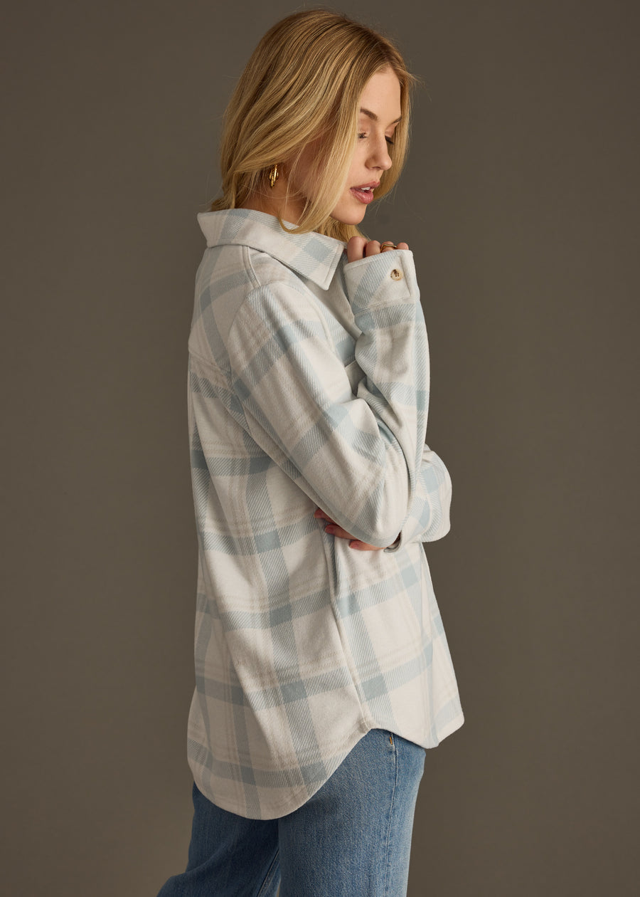 A woman with long blonde hair wears the Jules Super Soft Button Up by panacheaccessories in dusty teal plaid with blue jeans, standing sideways with crossed arms and looking slightly downward against a plain background.