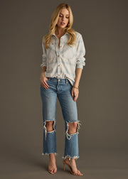 A woman with long blonde hair poses against a plain background wearing panacheaccessories’ Jules Super Soft Button Up in dusty teal plaid, paired with ripped blue jeans and nude high-heeled sandals.