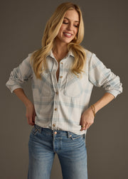 A smiling woman with long blonde hair wears the panacheaccessories Jules Super Soft Button Up and blue jeans, standing against a plain gray background with her hands on her hips.