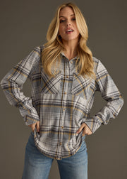 A woman with long blonde hair wears the Ozzy Super Soft Button Up by panacheaccessories—a gray, white, and yellow plaid long sleeve shirt—paired with blue jeans, standing hands on hips against a plain dark background.