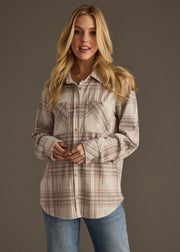 A woman with long blonde hair wears the Lia Super Soft Button Up by panacheaccessories in plaid beige and pink, paired with light blue jeans, standing against a plain gray background and looking at the camera with a neutral expression.