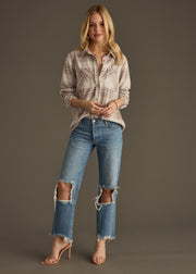 A woman with long blonde hair poses against a plain background, wearing the Lia Super Soft Button Up from panacheaccessories, ripped blue jeans with frayed hems, and nude high-heeled sandals.
