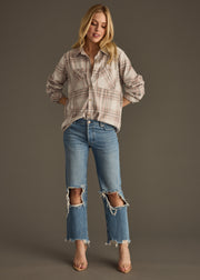 A woman with long blonde hair stands against a plain background wearing panacheaccessories’ Lia Super Soft Button Up and ripped blue jeans with frayed hems. She has open-toe heels, hands in her pockets, and a relaxed expression.