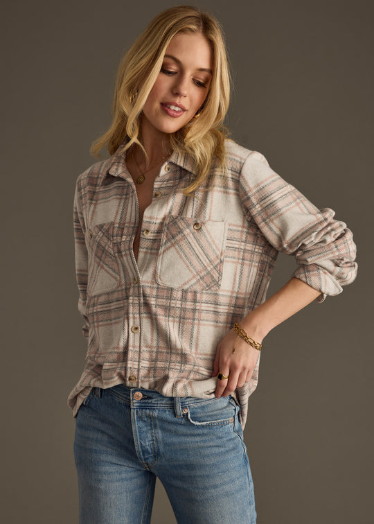 A woman wearing the panacheaccessories Lia Super Soft Button Up and blue jeans stands against a plain background, looking down with a slight smile and one hand in her pocket.