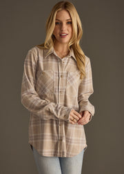 A woman with long blonde hair wears the panacheaccessories Hilarie Super Soft Button Up in beige and gray plaid with light blue jeans, standing against a plain brown background.