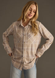 A woman with long blonde hair models the panacheaccessories Hilarie Super Soft Button Up, featuring long sleeves and plaid pattern, over light blue jeans, standing with hands on hips against a plain dark background.