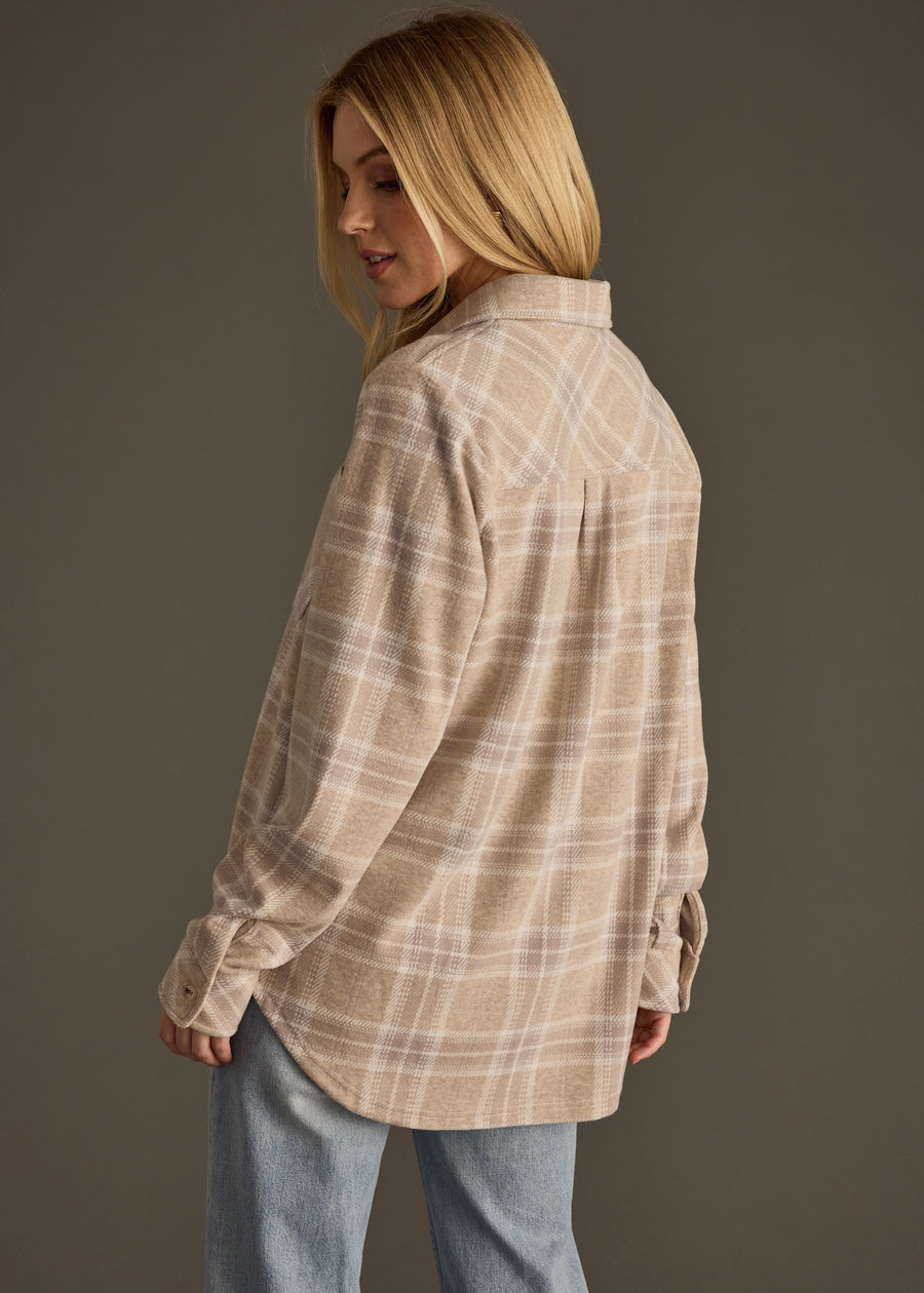 A woman with long blonde hair, dressed in the panacheaccessories Hilarie Super Soft Button Up and light blue jeans, stands slightly turned away from the camera against a plain dark background.