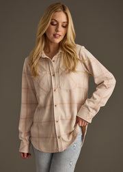 A woman with long blonde hair wears the Blaire Super Soft Button Up by panacheaccessories and light blue jeans, standing against a dark background and looking down with a slight smile.