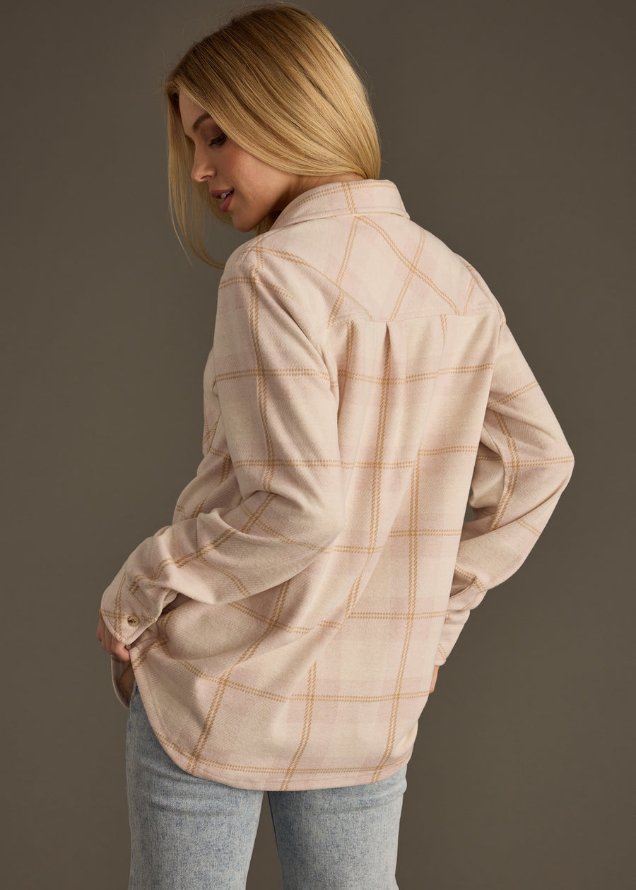 A woman with long blonde hair models the panacheaccessories Blaire Super Soft Button Up, paired with light blue jeans. She stands with her back to the camera, looking over her shoulder against a plain background.