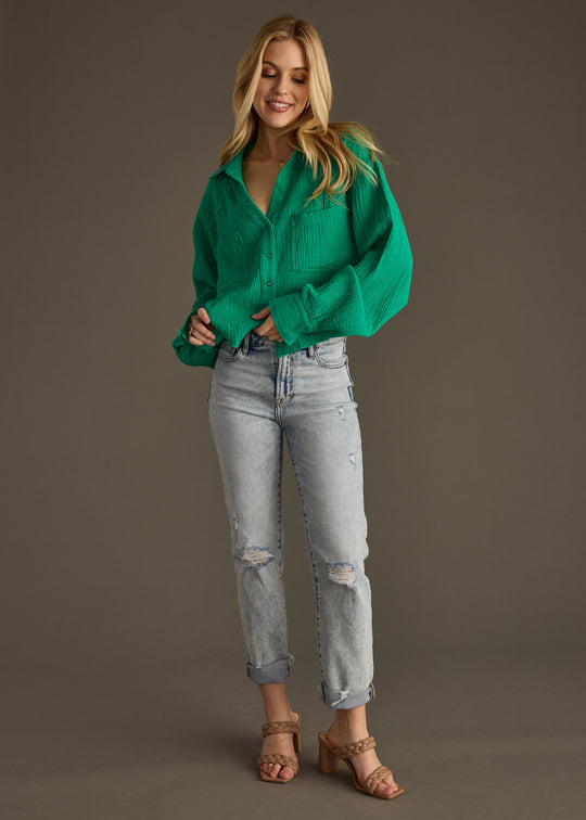 A woman smiles against a plain background, wearing the Wild Heart Button Up - Green from panacheaccessories, styled with light-wash ripped jeans and tan heeled sandals.