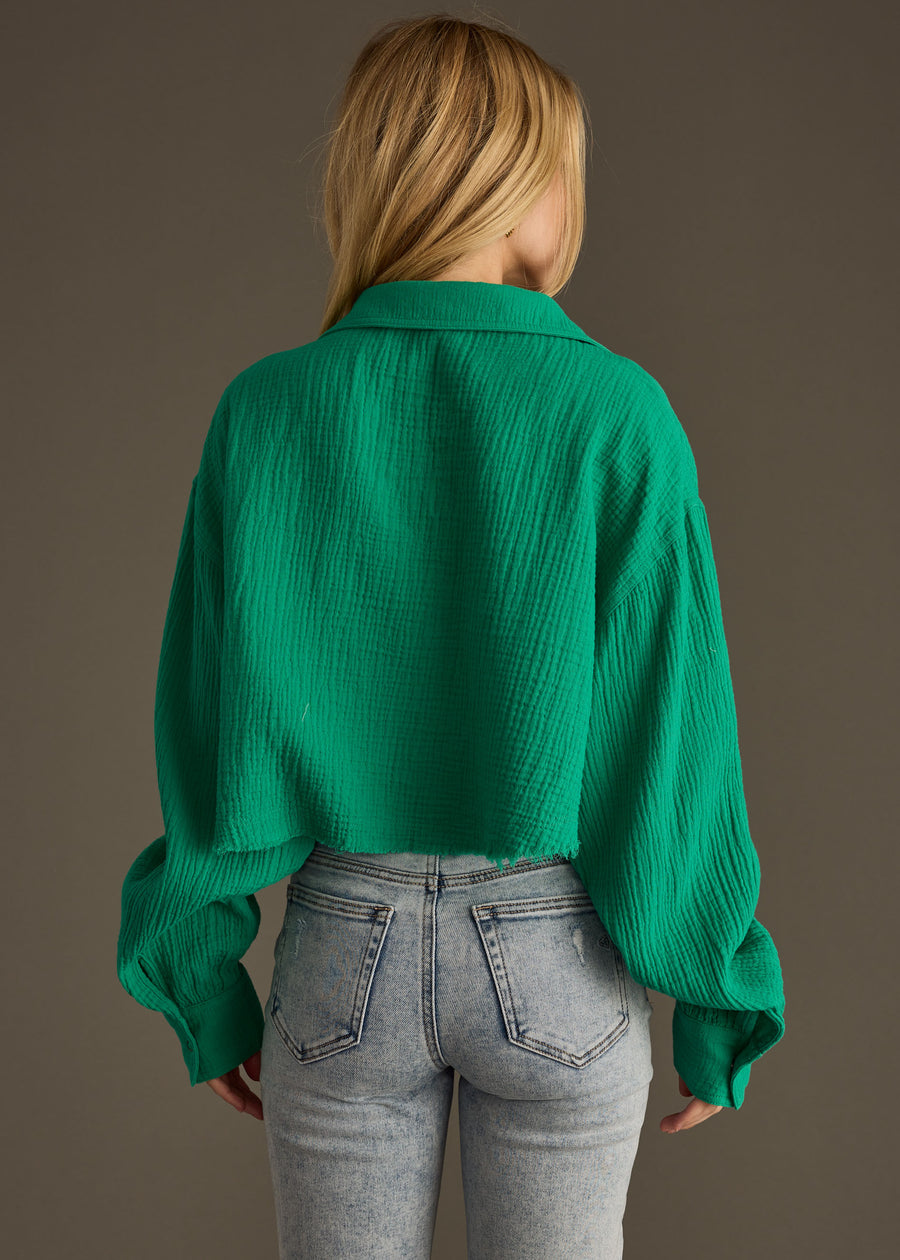 A person with long blonde hair is shown from the back, wearing the "Wild Heart Button Up - Green" by panacheaccessories in an oversized fit and high-waisted light blue jeans against a plain brown background.