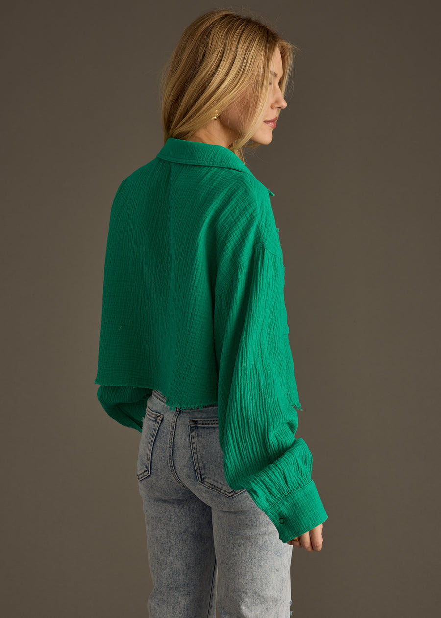 A person with long blonde hair wears the Wild Heart Button Up in green by panacheaccessories, styled oversized with light-wash jeans, standing sideways against a plain gray background.