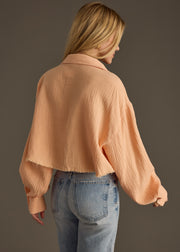 A woman with long blonde hair, seen from behind, wears the panacheaccessories Wild Heart Button Up - Orange with an oversized boxy fit and high-waisted light blue jeans against a plain dark background.